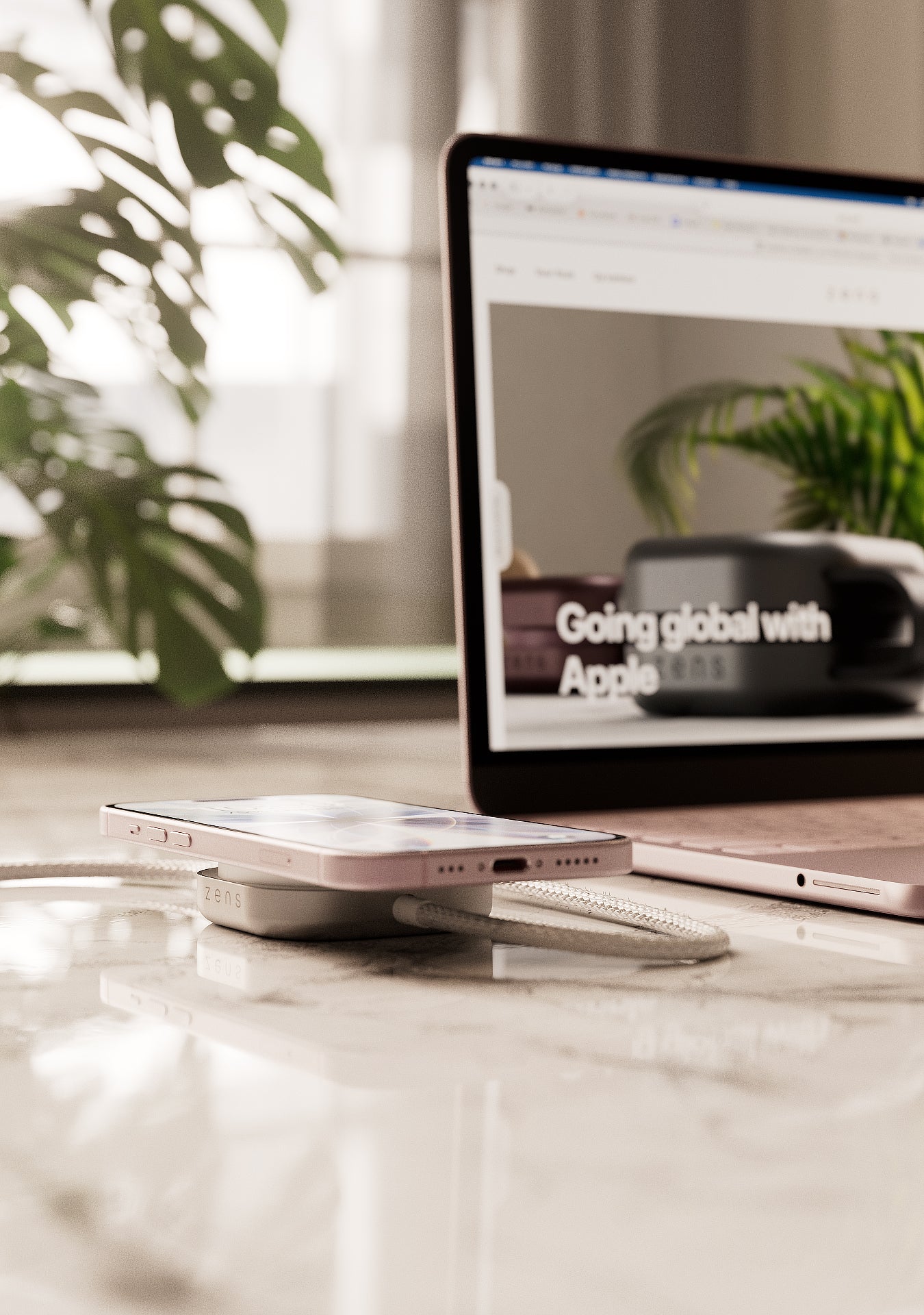 Wireless charging cable connected to a MacBook Neo charging an iPhone on a desk