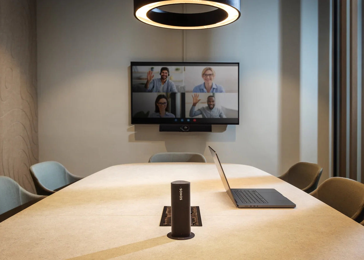 Office meeting room table with two wireless chargers, a Sonos speaker, a laptop, and a smartphone charging.
