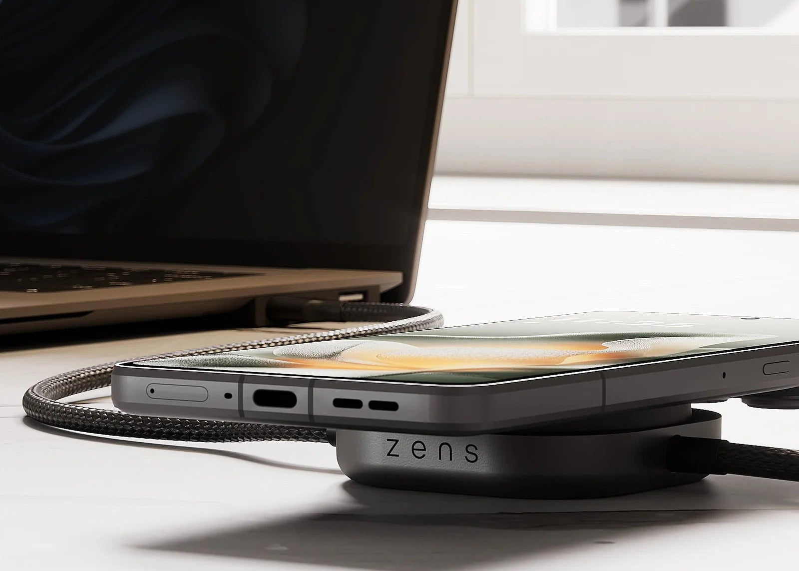 USB C to C charging cable charging a laptop and smartphone with wireless charging devices on a desk in a home office