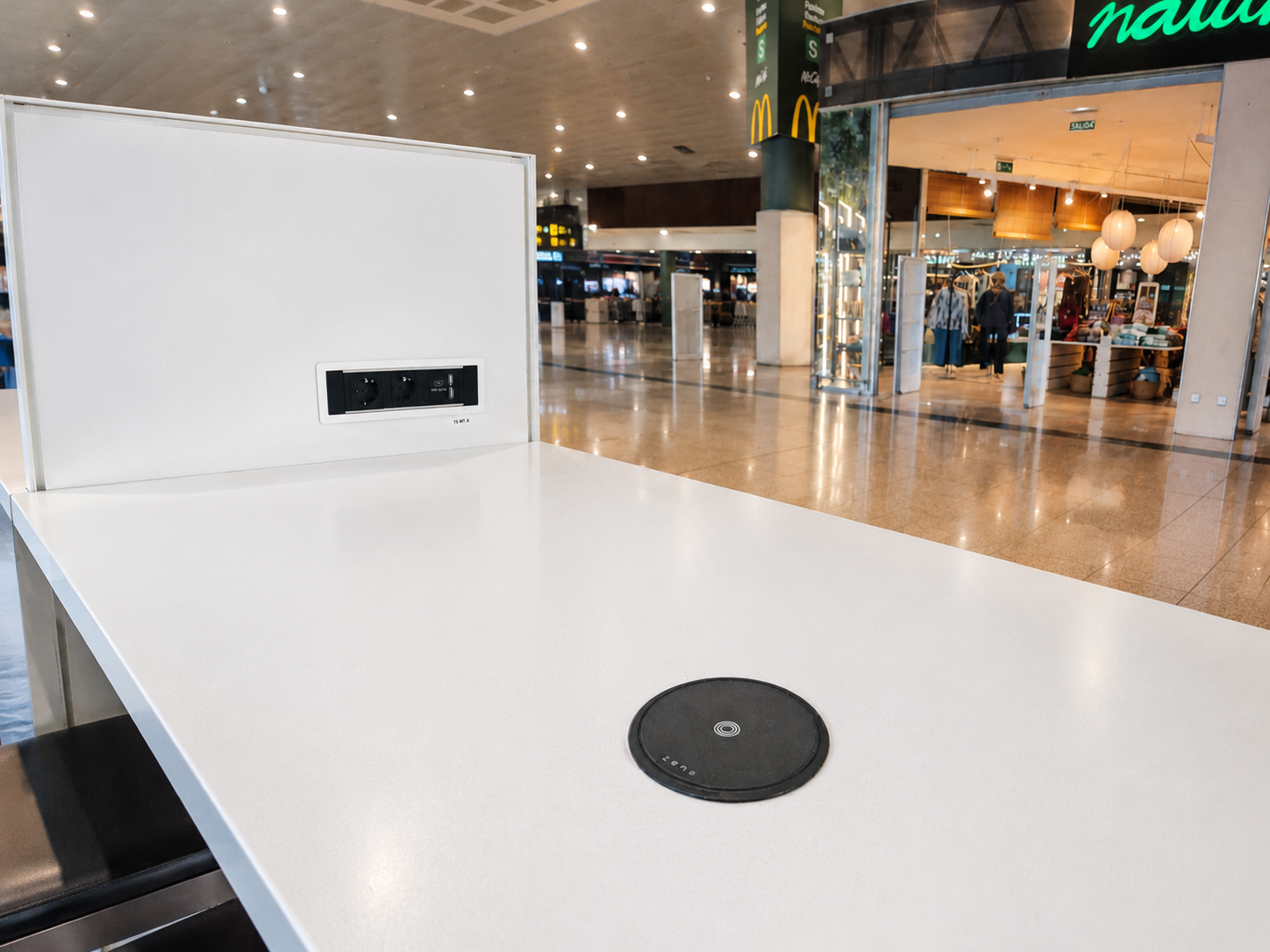 Built in wireless charger integrated into a table at an airport charging a smartphone.