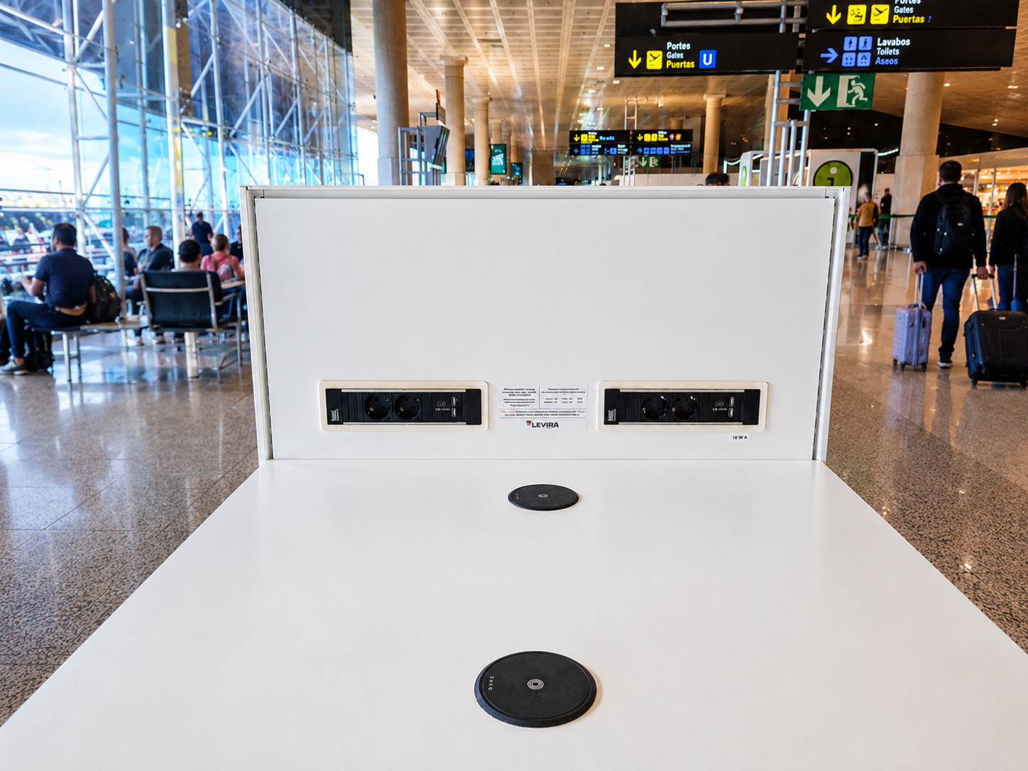 Built in wireless charger integrated into a table at an airport charging a smartphone.