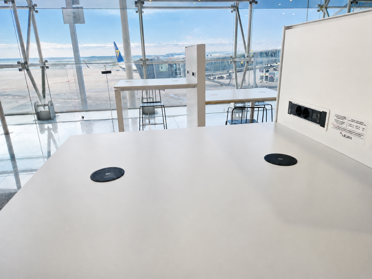 Built in wireless charger integrated into a table at an airport charging a smartphone.