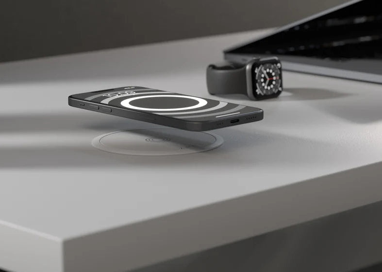 White Zens wireless charging puck charging an iPhone on a white desk with an Apple Watch in the background