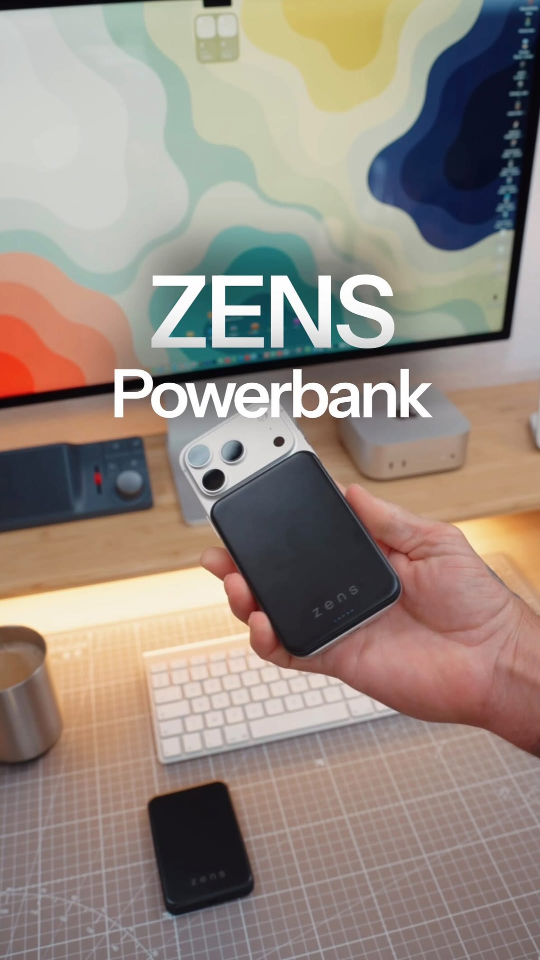 Black Zens MagSafe power bank attached to and charging a smartphone in a home office setting.