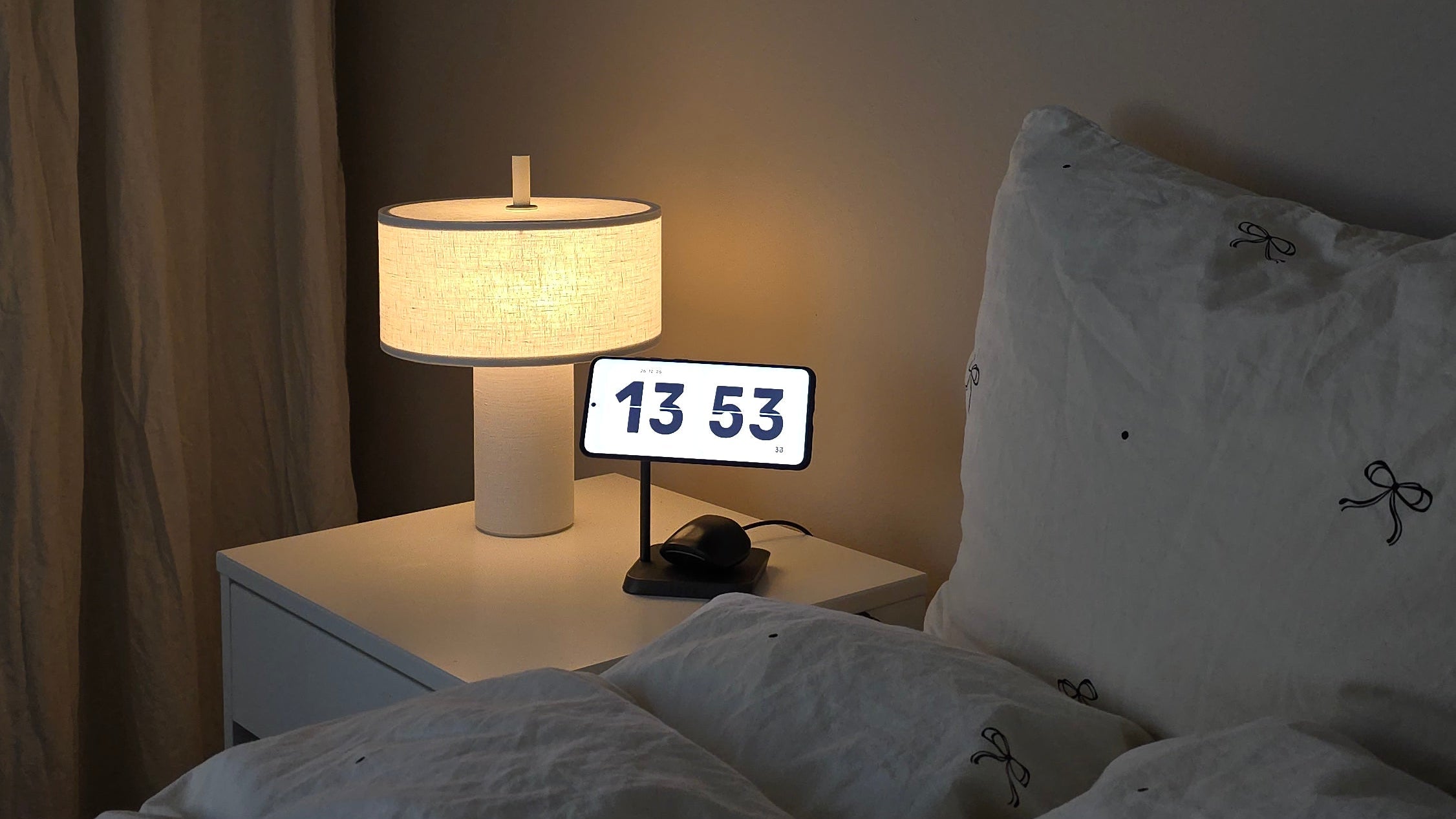 Zens 2 in 1 wireless charger charging a Samsung phone displaying a clock and wireless earbuds on a bedside table in a bedroom