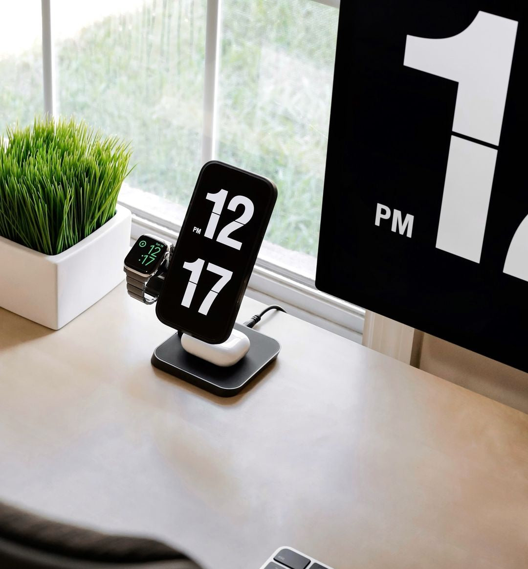 Zens Office Charger Pro 3 wirelessly and magnetically charging a smartphone displaying a clock, AirPods and Apple Watch in a lifestyle setting.