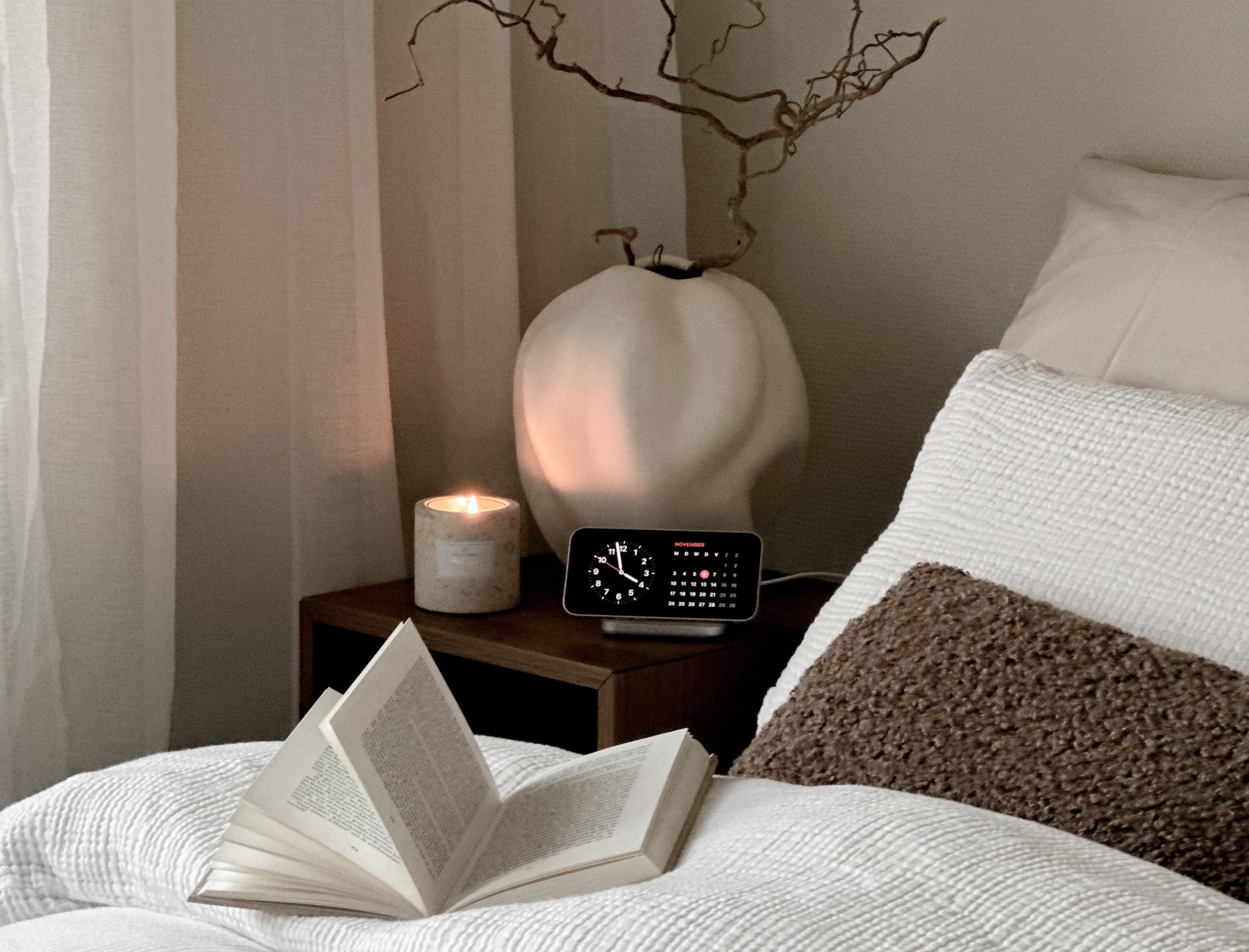 Magnetic nightstand charger charging a smartphone displaying a clock next to a bed.