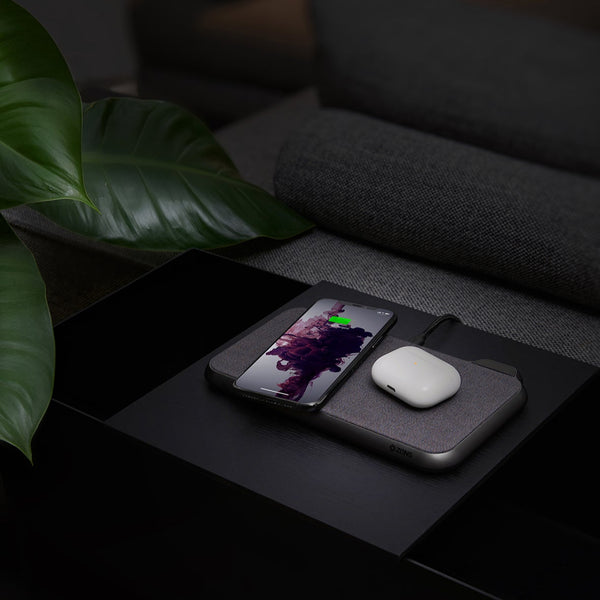 Smartphone and wireless earbuds on a dark surface with a plant in the corner