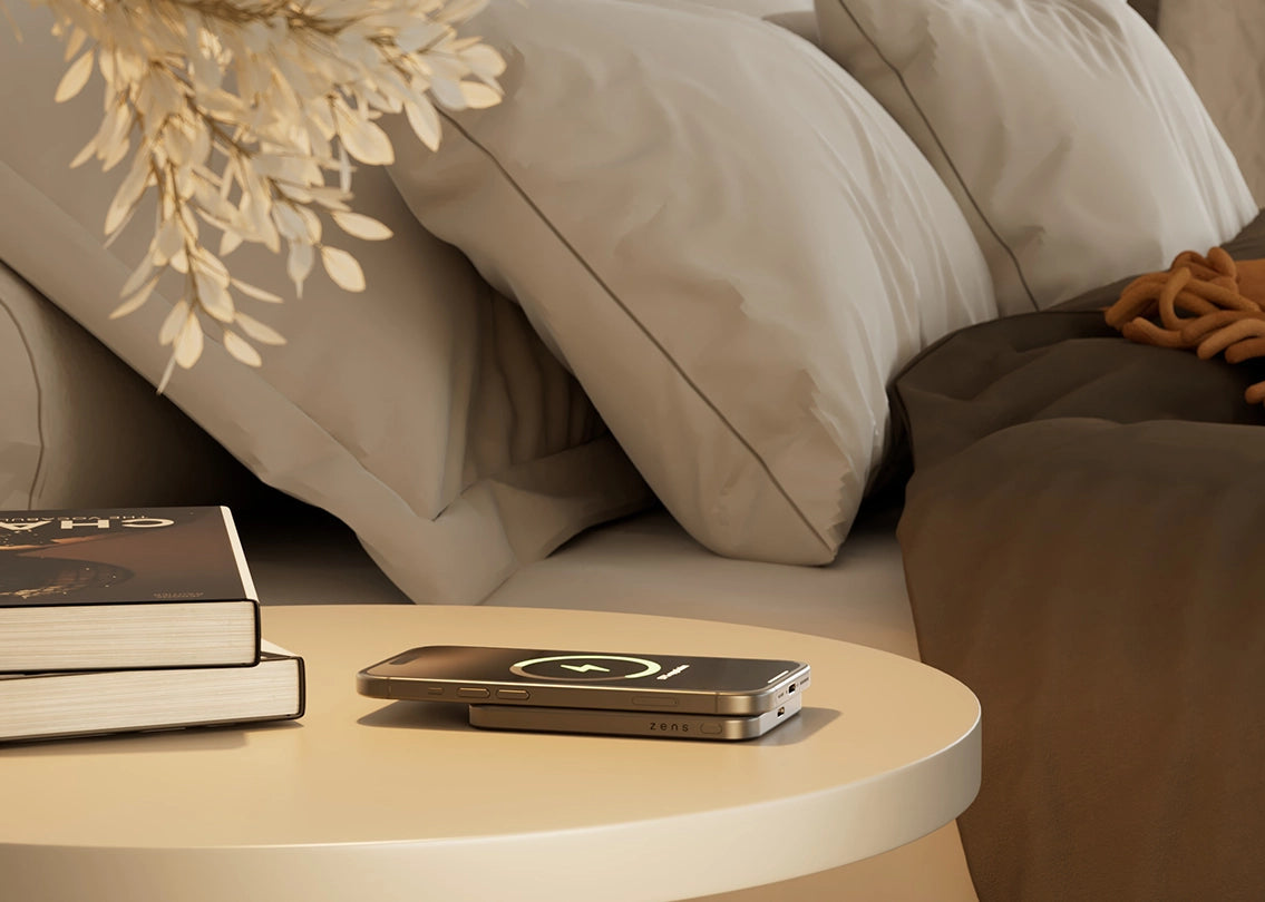MagSafe power bank charging a smartphone on a bedroom nightstand in a lifestyle setting.