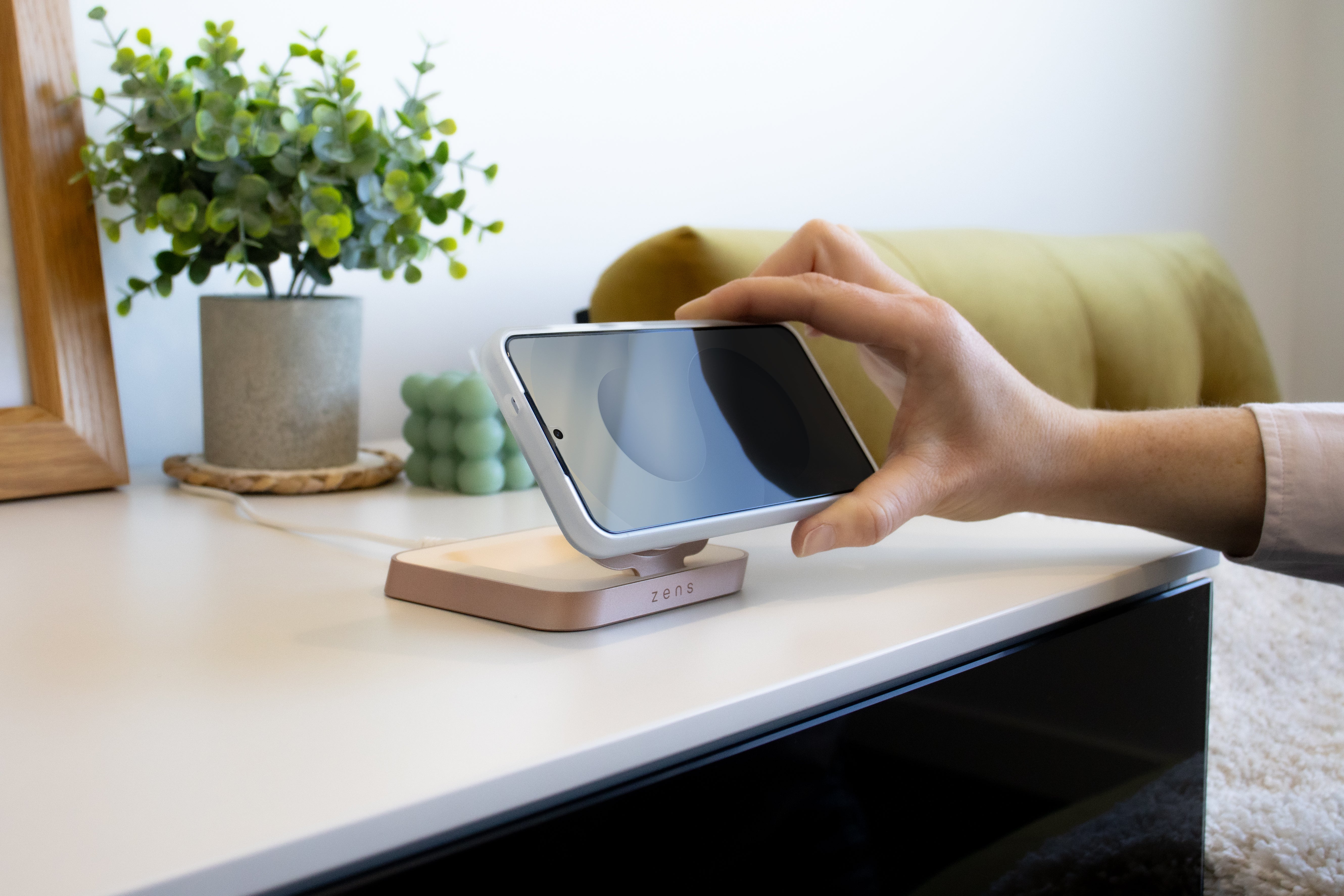 Woman placing a Samsung phone on a Zens magnetic nightstand charger on a living room table