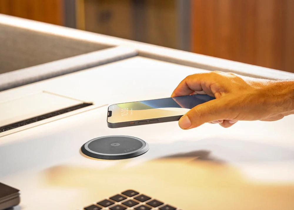 Black and white wireless charging puck charging a smartphone in an office setting.