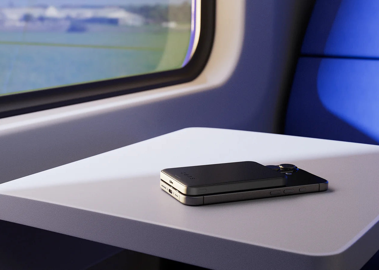 Black semi solid state MagSafe power bank charging a smartphone on a train.