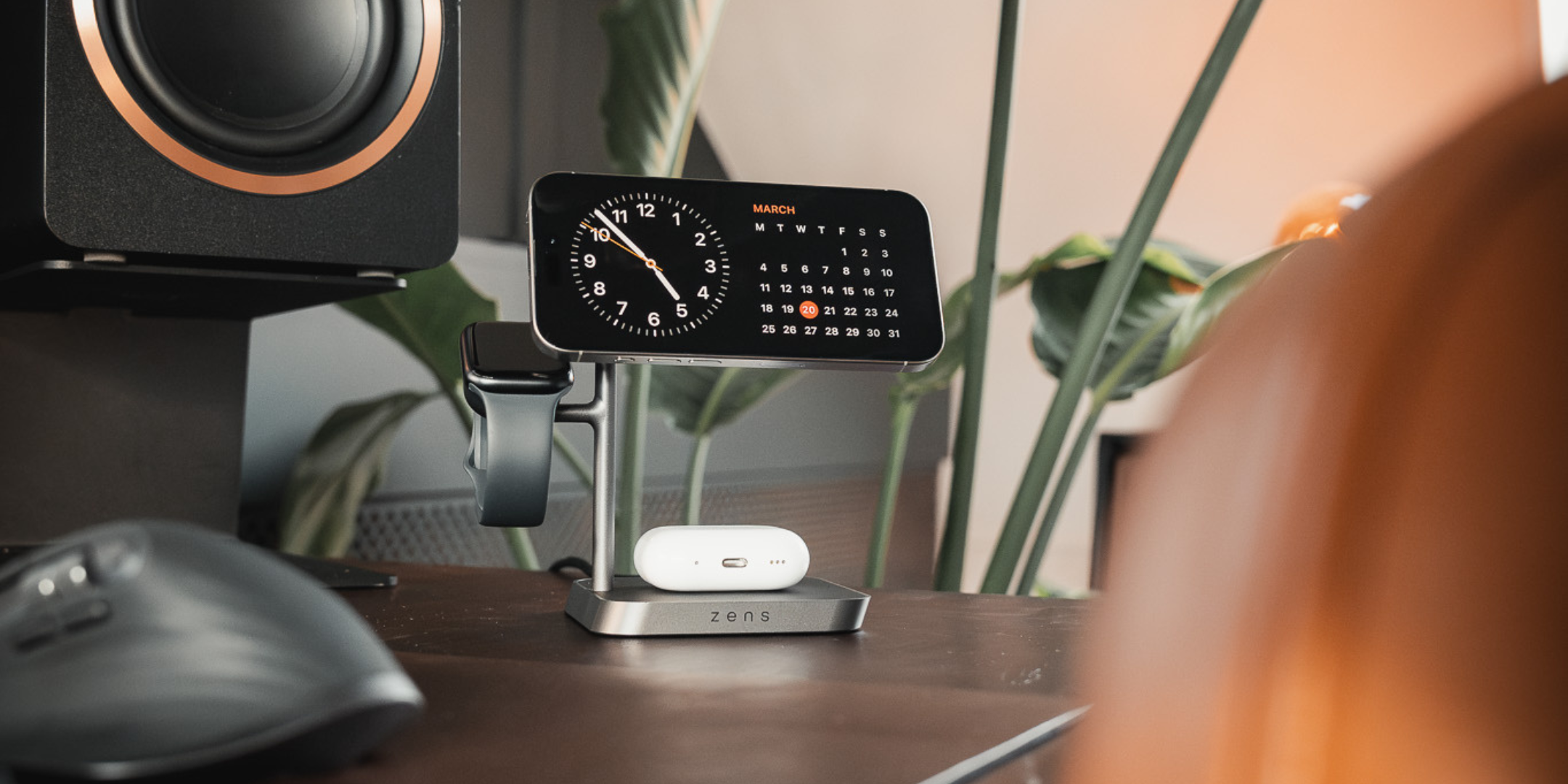 Zens Office Charger Pro 3 wirelessly and magnetically charging a smartphone displaying a clock, AirPods and Apple Watch in a lifestyle setting.